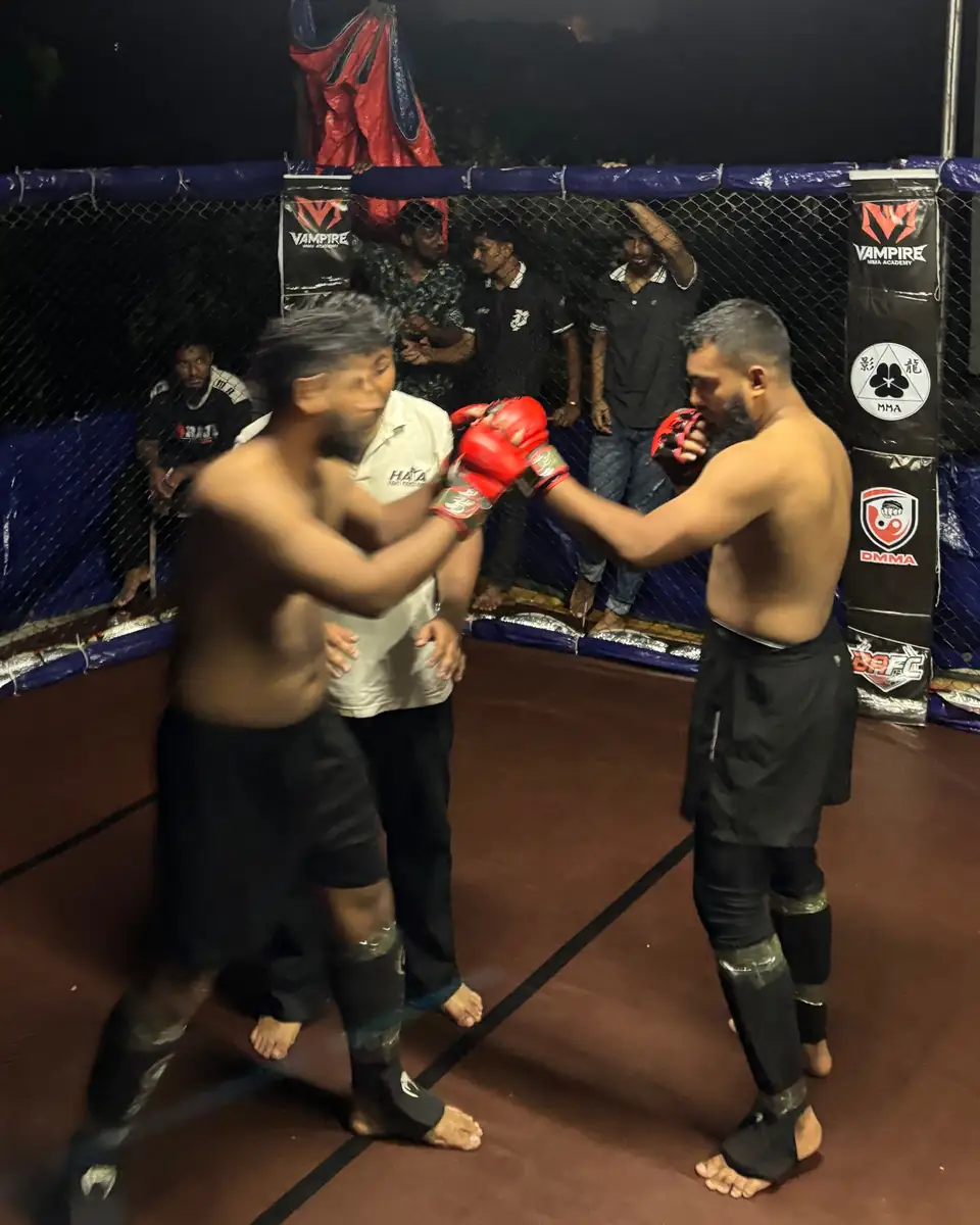 Two fighters trade punches in the cage with the referee between them